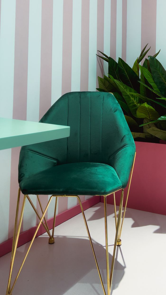 Sophisticated green velvet chair with gold legs in a chic interior setting enhanced by striped walls.